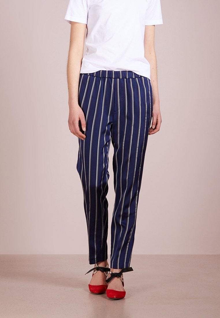 Námořnické pruhované kalhoty s uvolněným střihem, s bílými vertikálními pruhy, elastickým pasem a hladkou texturou látky. Červené boty na šněrování.