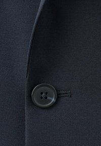 Tessuto di blazer blu navy con una texture liscia presenta un bottone rotondo nero con quattro fori. Il bottone è cucito sul capo nella parte anteriore.