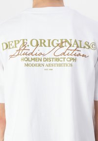 Hvit bomulls t-skjorte med stor, flerfarget tekst på baksiden: "DEPT. ORIGINALS Studio Edition" og andre design detaljer.