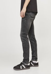 Jeans de mezclilla negra ajustados con textura deslavada, presentan un diseño clásico de cinco bolsillos y detalles de costura, combinados con zapatillas negras.