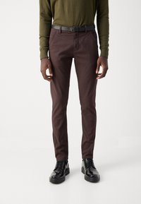 Καφέ βαμβακερό παντελόνι σε λεπτή γραμμή, με πλαϊνές τσέπες και λείες υφές. Συνδυασμένο με μαύρα παπούτσια και γκρι ζώνη.