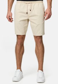 Beige bomulds shorts med elastisk talje og snoretræk, som har sidelommer, lige pasform og opfoldede benkanter. Kombineret med hvide sneakers.