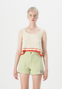 Kremfarget ribbestrikket crop-top med røde striper i kanten, kombinert med lysegrønne kordfløyelsshorts som har sidelommer og et merkelapp.