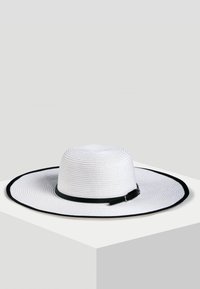 Szerokoskrzydły biały kapelusz ze słomy z teksturowaną powierzchnią, z czarnym paskiem i metalową klamrą. Płaski okrągły czubek i szeroki, zakrzywiony brzeg.