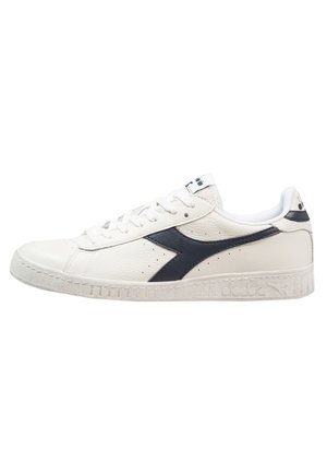 Sneaker bianco in pelle con accenti blu navy, suola testo, perforazioni e lacci bianchi piatti. Presenta un logo sulla linguetta e sul lato.