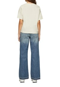 Crème korte mouwen t-shirt met een relaxte pasvorm, gecombineerd met wijde blauwe denim jeans met vervaagde accenten en ruwe zomen.