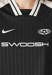 Svart sporttröja med vertikala ränder, vita detaljer, rund halsringning, "SWOOSH"-logotyp och en fotbollsgrafik på bröstet.