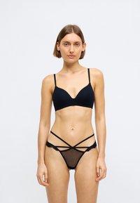 Μαύρο σετ εσωρούχων που περιλαμβάνει ένα λείο, αδιάβροχο σουτιέν με λεπτές τιράντες και ένα αντίστοιχο στρινγκ από δαντέλα και δίχτυ με διασταυρούμενες λεπτομέρειες.