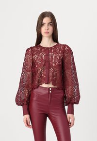 Burgundy lace cropped blouse with patterned sleeves and button closure. Paired with matching high-waisted fitted pants. Textured design throughout.