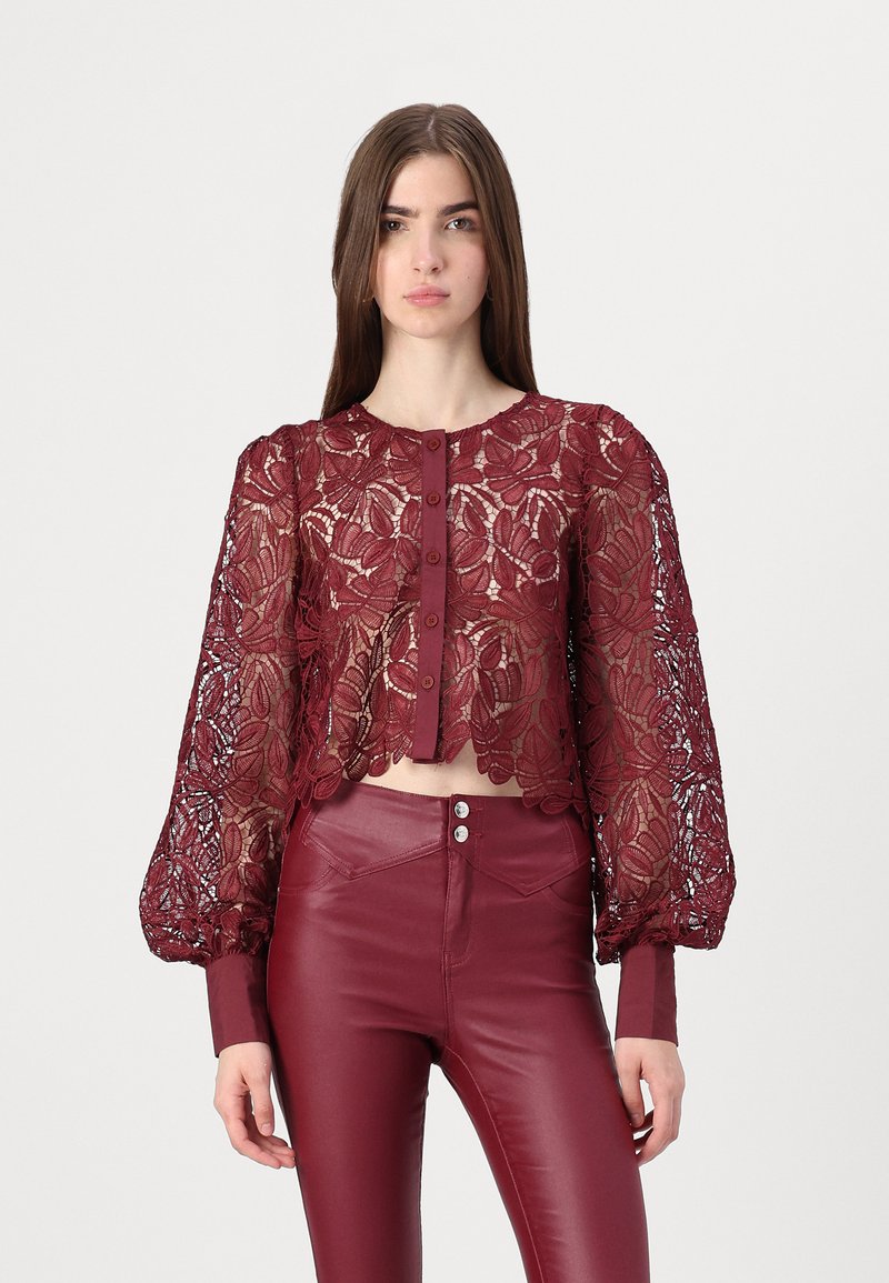 Burgundy lace cropped blouse with patterned sleeves and button closure. Paired with matching high-waisted fitted pants. Textured design throughout.