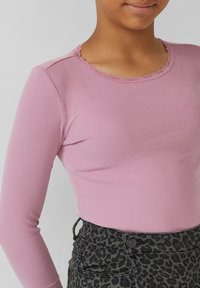 Kind dat een rozenrode ribbenpull met kantafwerking bij de hals draagt, samen met donkergrijze broek met luipaardprint.