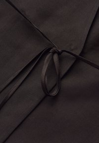 Dark fabric folded with a thin strap tied in a simple loop knot on top, highlighting texture and stitching details.