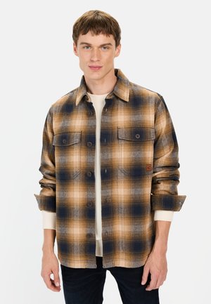 Bruine en marineblauwe geruite flanellen shirt met twee borstzakken, knopen aan de voorkant en Contrasterende witte binnenmanchetten. Zachte textuur.