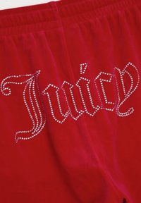 Shorts rossi in velluto con la scritta "Juicy" adornata di strass in un elegante carattere decorativo. Tessuto morbido, vita elastica e design dettagliato.