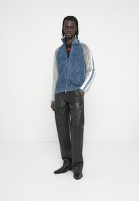 Ζακέτα με φερμουάρ σε μπλε και γκρι χρώμα με ριγέ μανίκια, συνδυασμένη με μαύρο δερμάτινο παντελόνι. Λείο ύφασμα και εφαρμοστή γραμμή.