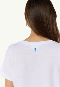 White cotton t-shirt with a round neckline. The back features a small blue tag with the letters "CI" on it. Smooth texture, relaxed fit.