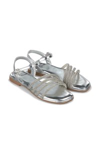 Silberne Sandalen mit flacher Sohle verfügen über mehrere metallische Riemen, einen verstellbaren Knöchelriemen und eine glatte reflektierende Oberfläche.
