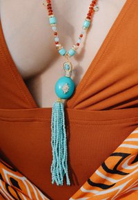 Collier en perles turquoise et rouge avec un grand pendentif turquoise et des accents dorés, comportant un pompon de petites perles.