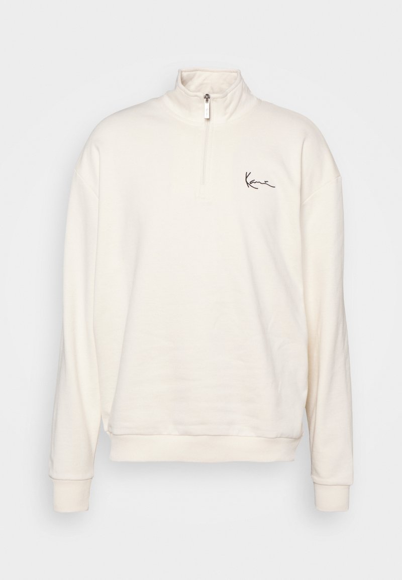 Felpa color crema con colletto alto, zip frontale a metà, maniche lunghe, polsini a costine e un semplice logo nero sul petto.