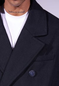 Manteau en laine mélangée bleu marine avec un design de blazer, des revers pointus, une fermeture à bouton unique et une finition texturée. T-shirt blanc en dessous.