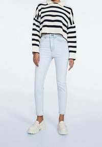 Pruhovaný krémový a námořnický svetr, zkrácená délka, vysoké světle modré džíny a masivní bílé mokasíny s drsnou podrážkou. Čistý design, ležérní střih.