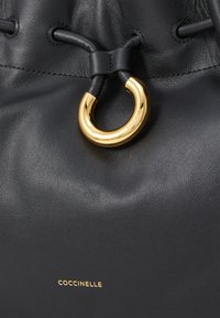 Borsa a tracolla in pelle nera con superficie texture, dotata di un anello in metallo dorato e chiusura con coulisse. Logo dorato nella parte inferiore.