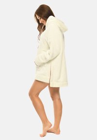 White, fluffy hooded robe with a plush texture, side slits, and a relaxed fit, featuring a visible kangaroo pocket and rolled cuffs.