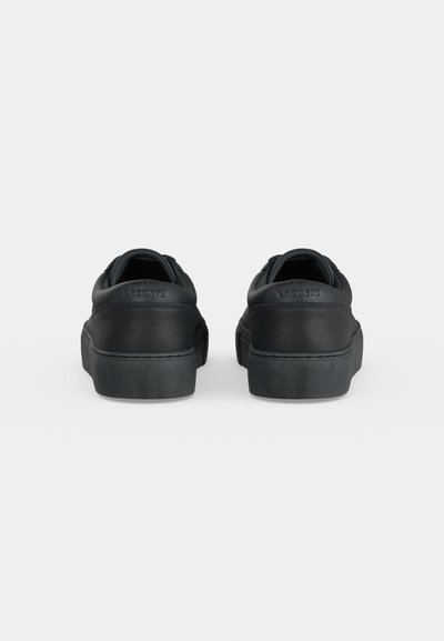 Двойка черни маратонки Lacoste, показани отзад, с дебело ходило и релефно лого на езичето на петата.