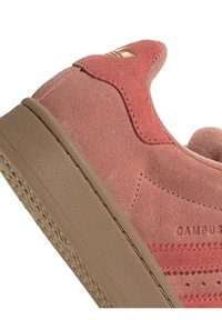 Gros plan d'une basket en suède rose avec une semelle marron texturée, montrant des détails cousus et un texte partiellement embossé "CAMPUS".