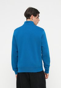 Μπλε πουλόβερ φούτερ με μακριά μανίκια και γιακά, φτιαγμένο από μαλακό ύφασμα. Διαθέτει ribbed μανίκια και στρίφωμα, με απλό σχέδιο.