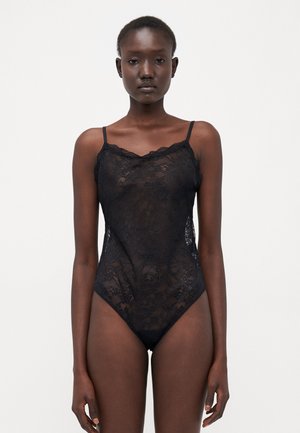 Černý krajkový body s tenkými ramínky a zvlněnými okraji. Obsahuje květinový vzor a vysoký střih na nohách. Průhledná textura a přiléhavý design.