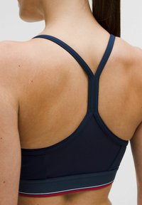 Granatowy stanik sportowy wykonany z elastycznego materiału, z plecami typu racerback i kontrastującą taśmą w czerwono-białe paski.