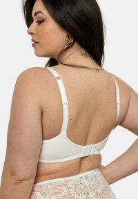 Soutien-gorge blanc avec des bretelles ajustables et une fermeture à crochets, présentant un tissu lisse et un design sobre. Dentelle visible en bas.