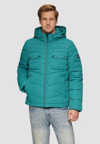 Teal gevoerde jas met een capuchon, ritssluiting en twee voorzakken met klep. Kenmerkt zich door horizontale stiksels en een logopatch op de mouw.
