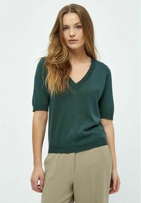 Suéter verde de manga corta y escote en V en una tela ligera y texturizada, combinado con pantalones beige neutros, creando una silueta relajada.