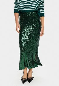 Green sequin pencil skirt with a side slit, featuring a smooth, shiny texture and a fitted silhouette, paired with black pointed-toe heels.