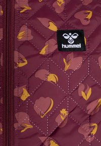 Vatterad burgunderröd jacka med blommönster i gult och rosa. Har en svart etikett med "hummel"-logotyp och en dragkedjestängning.