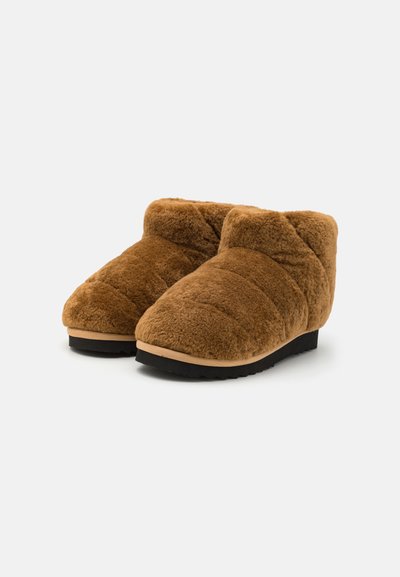 Barna, plüss, bokáig érő papucsok, texturált, steppelt felülettel és kontrasztos fekete gumi talppal. Belső használatra tervezve.
