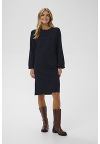 Robe tricotée bleu marine à manches longues, encolure ronde et coupe décontractée, assortie à des bottes brunes montantes. Design simple et polyvalent.