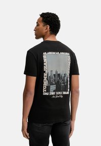 Camiseta negra de manga corta con un diseño gráfico de un horizonte urbano en la parte de atrás, con acentos de texto en blanco y beige.