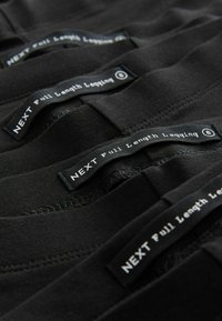 Zwarte full-length leggings gestapeld met zichtbare merknamen. Het materiaal lijkt rekbaar met een soepele textuur en minimale stikseldetails.