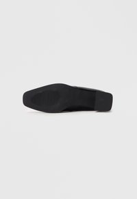 Zapato de tacón alto negro con parte superior lisa, punta afilada y suela texturizada. Presenta un diseño elegante y una estética minimalista.
