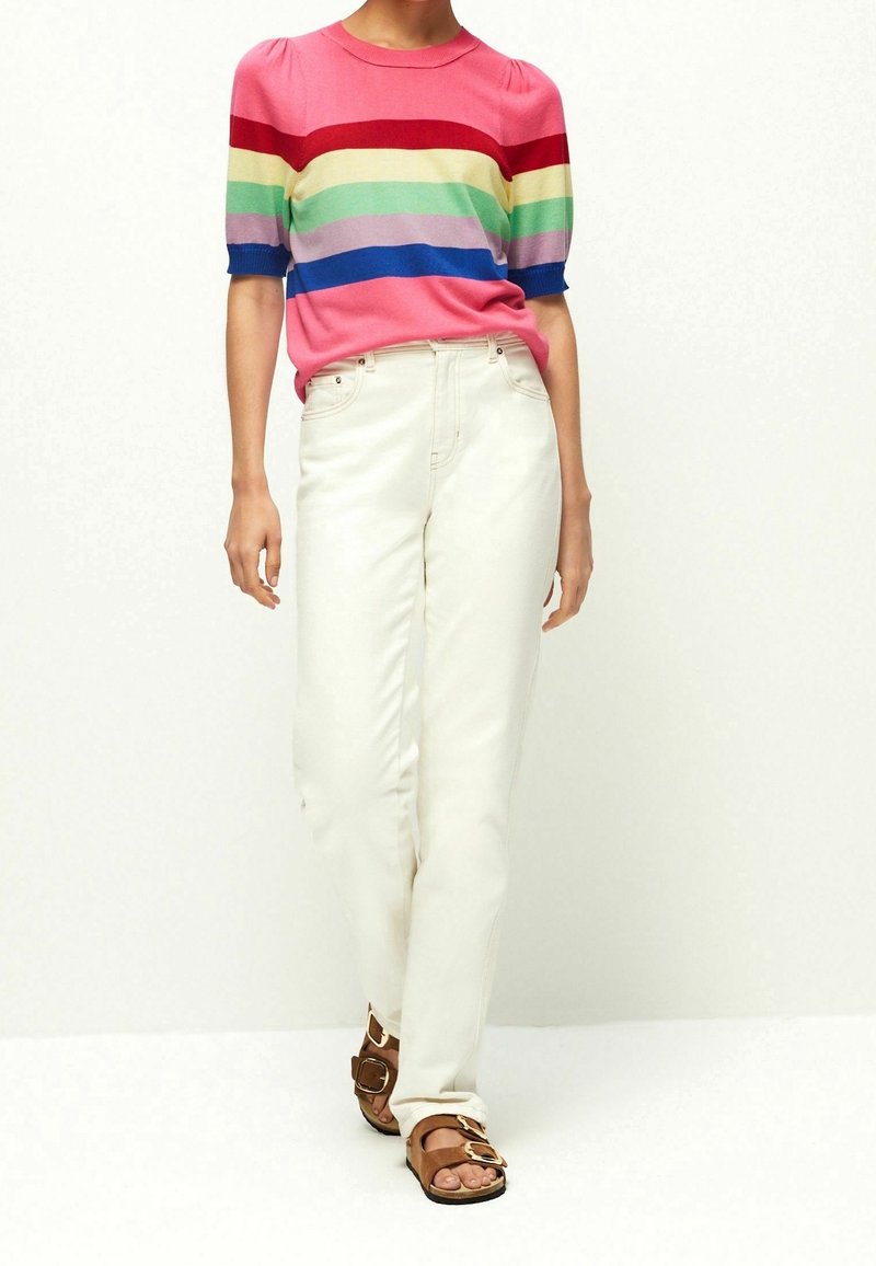 Stripet kortærmet sweater i pink, rød, blå, grøn og lavendel, parret med hvide straight-leg jeans og brune sandaler med spænder.