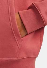 Felpa rustica rosa con orlo e polsini a costine, dotata di una tasca laterale e una texture liscia. Le cuciture in vista accentuano il design.