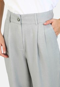 Light grey, tailored trousers with a high waist, pleats, and side pockets. Made of textured fabric; features a button closure.