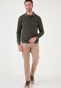 Donkergroen pullover met een kraag en drie knopen, gecombineerd met lichtbeige broeken en multikleurige sneakers. Eenvoudig, klassiek ontwerp.