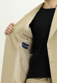 Blazer beige con un esterno tessurizzato, che presenta una tasca interna con bottone, fodera leggera e un'etichetta "Palo Club".