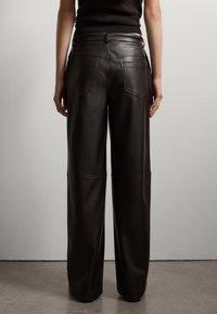 Pantalons larges en cuir marron foncé, présentant une texture lisse, deux poches arrière et des coutures sur les jambes.