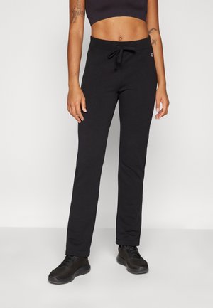 Svarte elastiske sweatpants med lynlås, lige ben-design og sidelommer. Båret med teksturerede sorte sneakers.