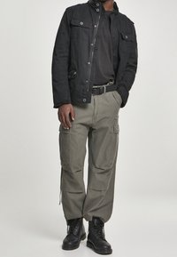 Svart jacka i bomullsblandning med framfickor, kombinerad med löst sittande olivgröna cargobyxor och svarta snörstövlar.